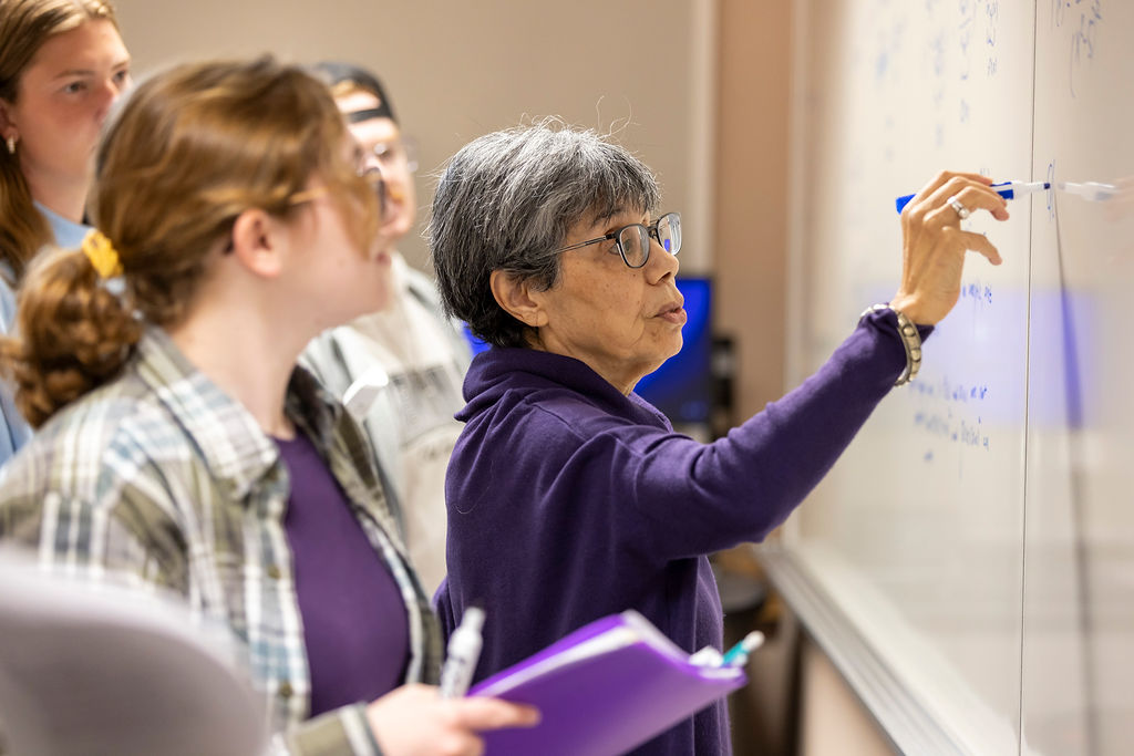 An Illinois Wesleyan professor working through a problem at the whiteboard with students