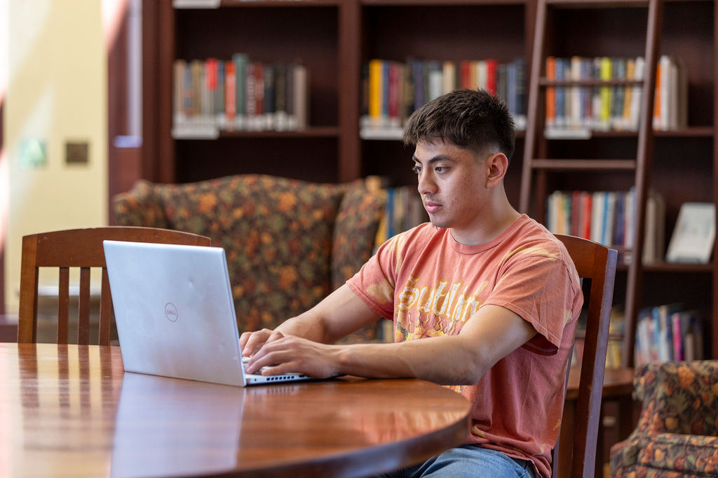 An Illinois Wesleyan student studying with a laptop in the campus library